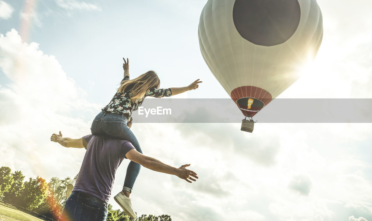 Couple enjoying on field while hot air balloon flying in sky