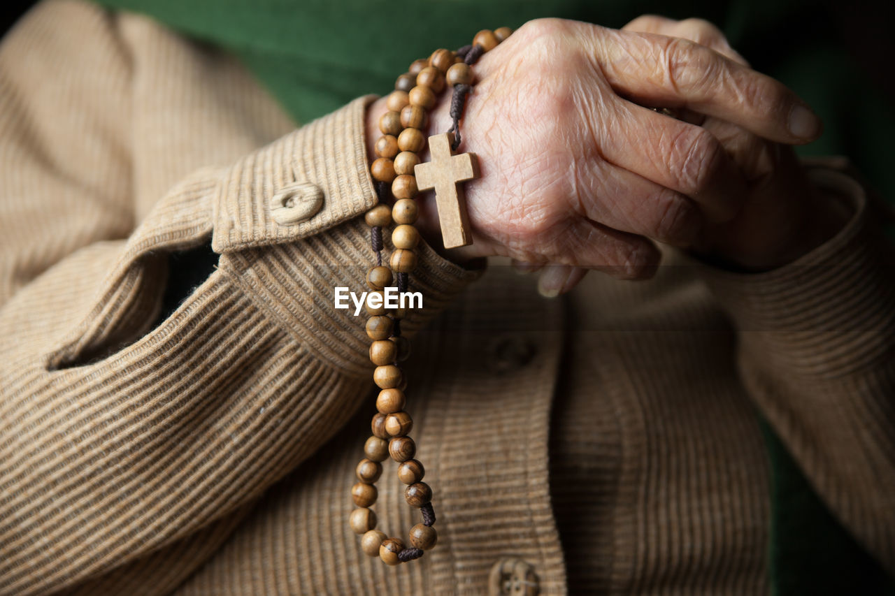Midsection of senior woman holding wooden rosary beads with cross