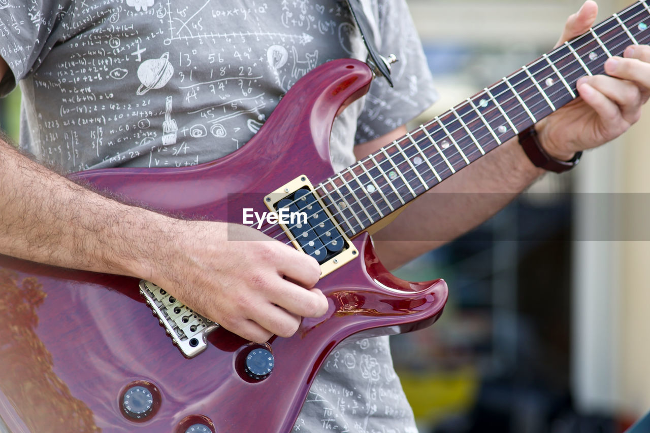 MIDSECTION OF MAN PLAYING GUITAR AGAINST BLURRED BACKGROUND