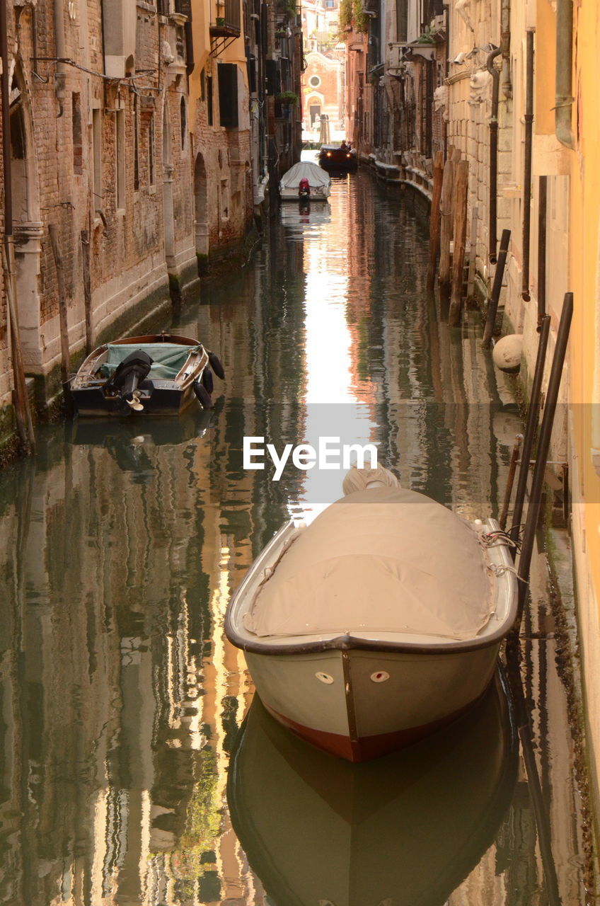 Boats moored in canal amidst buildings in city