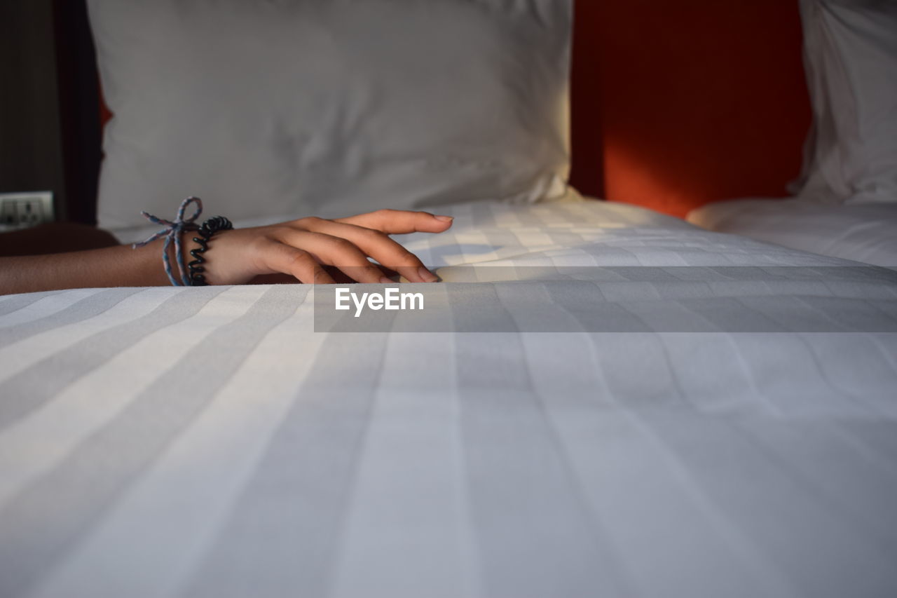 Cropped hand of woman on bed at home