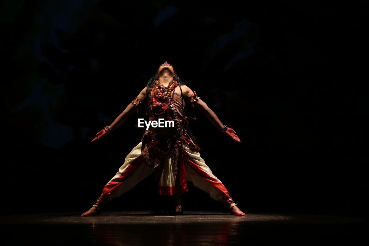 Full length of man wearing shiva costume performing on stage in dark