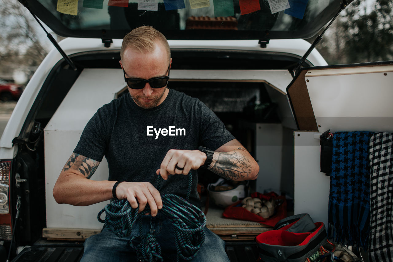 Man sitting on back of truck preparing rock climbing ropes