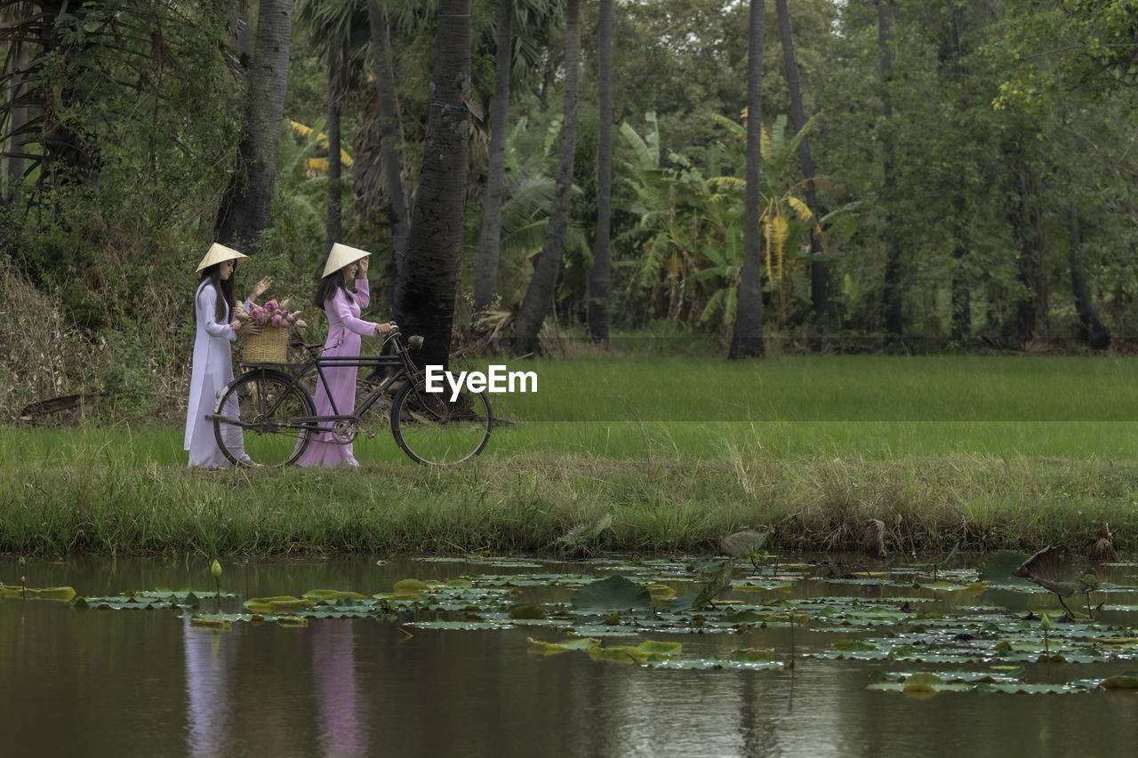 Female friends walking with bicycle by lake on land