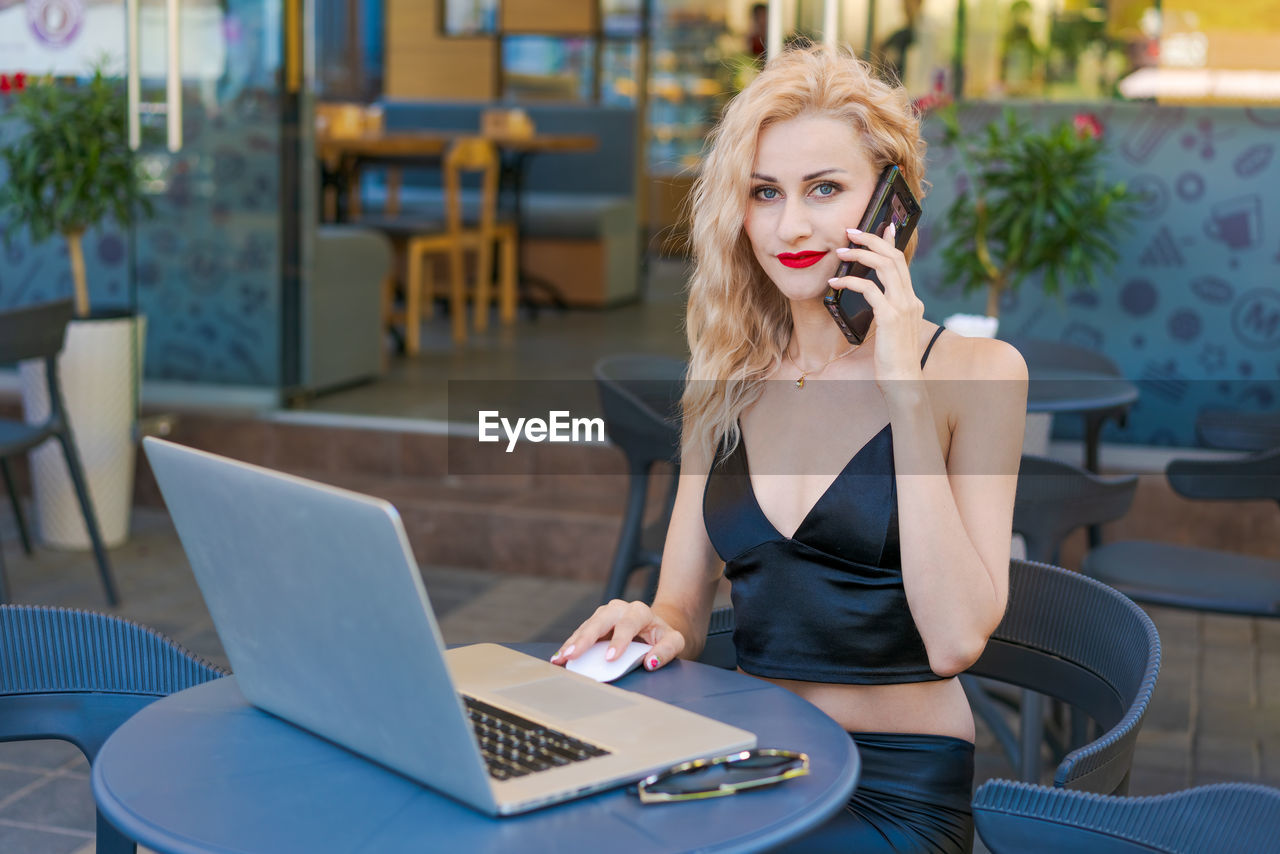 Beautiful woman in glasses sits at table in a street cafe and works on tablet