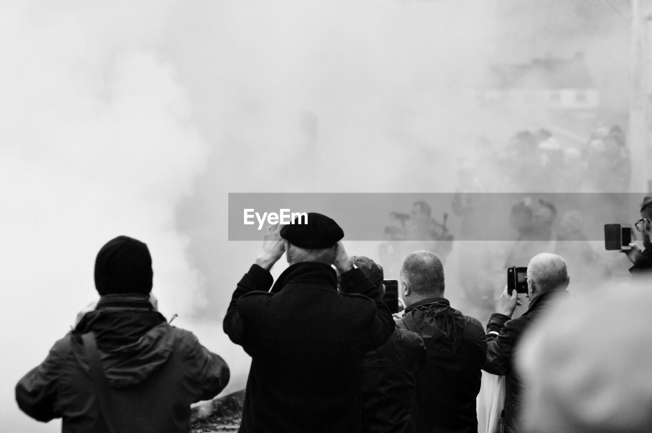 Rear view of people against sky with smoke 