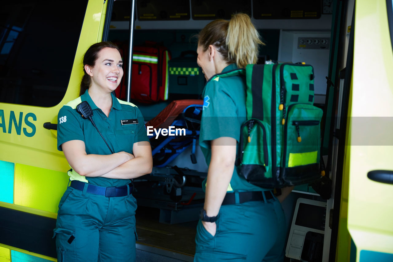 Smiling female paramedics talking while standing by ambulance in parking lot
