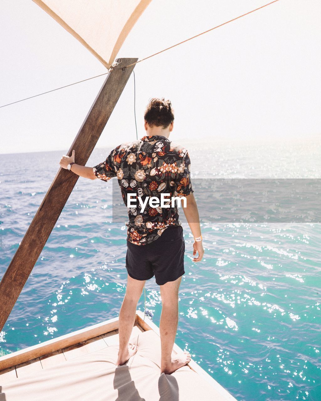 Rear view of man standing on pier while looking at sea against sky