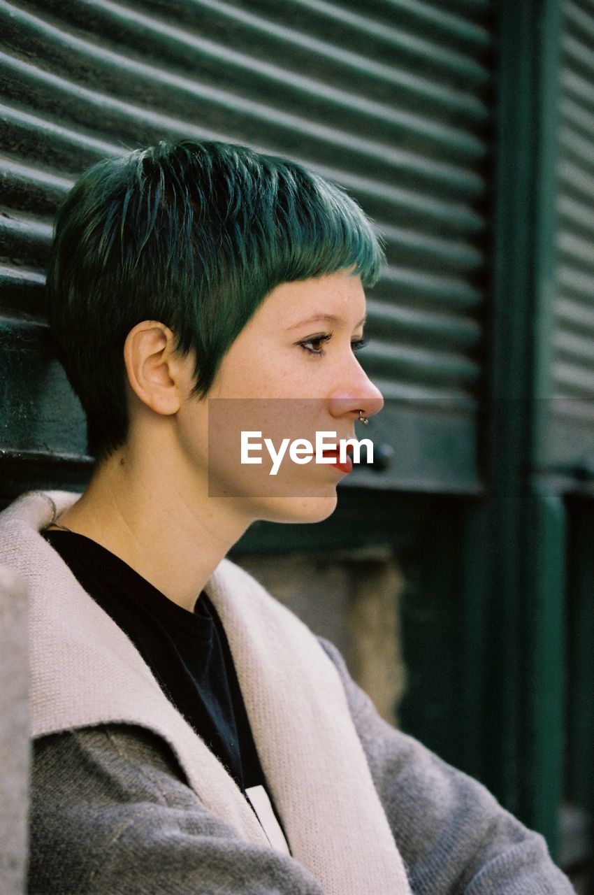 Side view of punk woman standing against green shutter