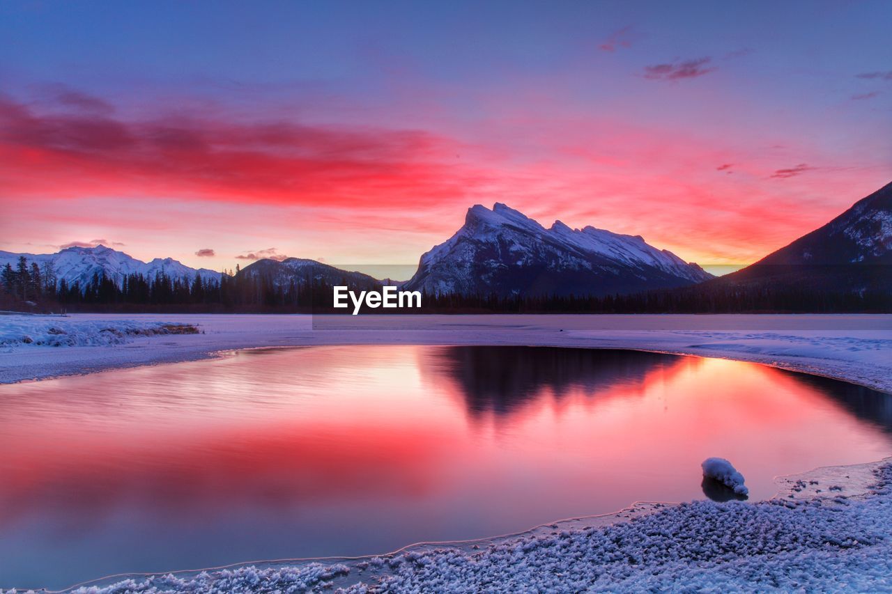 Scenic view of lake by snowcapped mountains against romantic sky