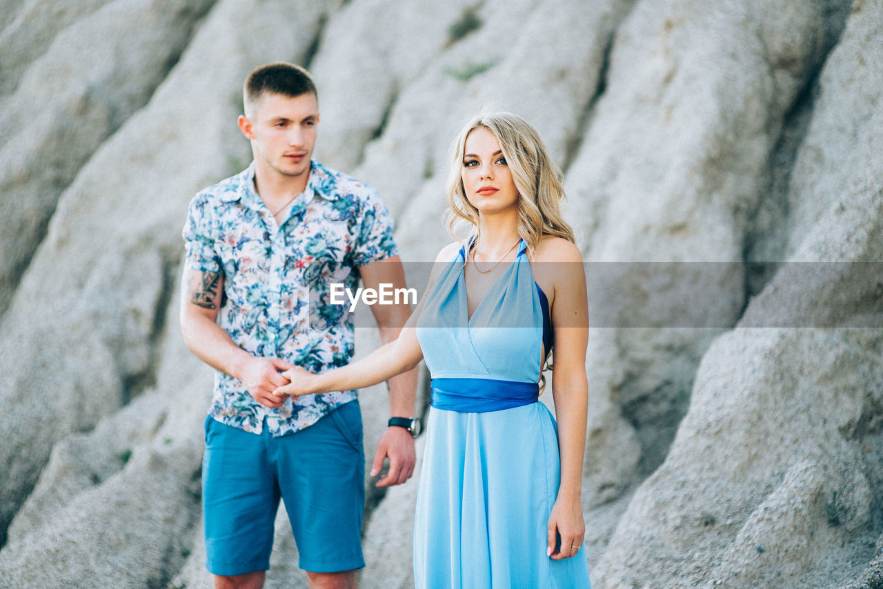 YOUNG COUPLE STANDING ON ROCK AGAINST WALL