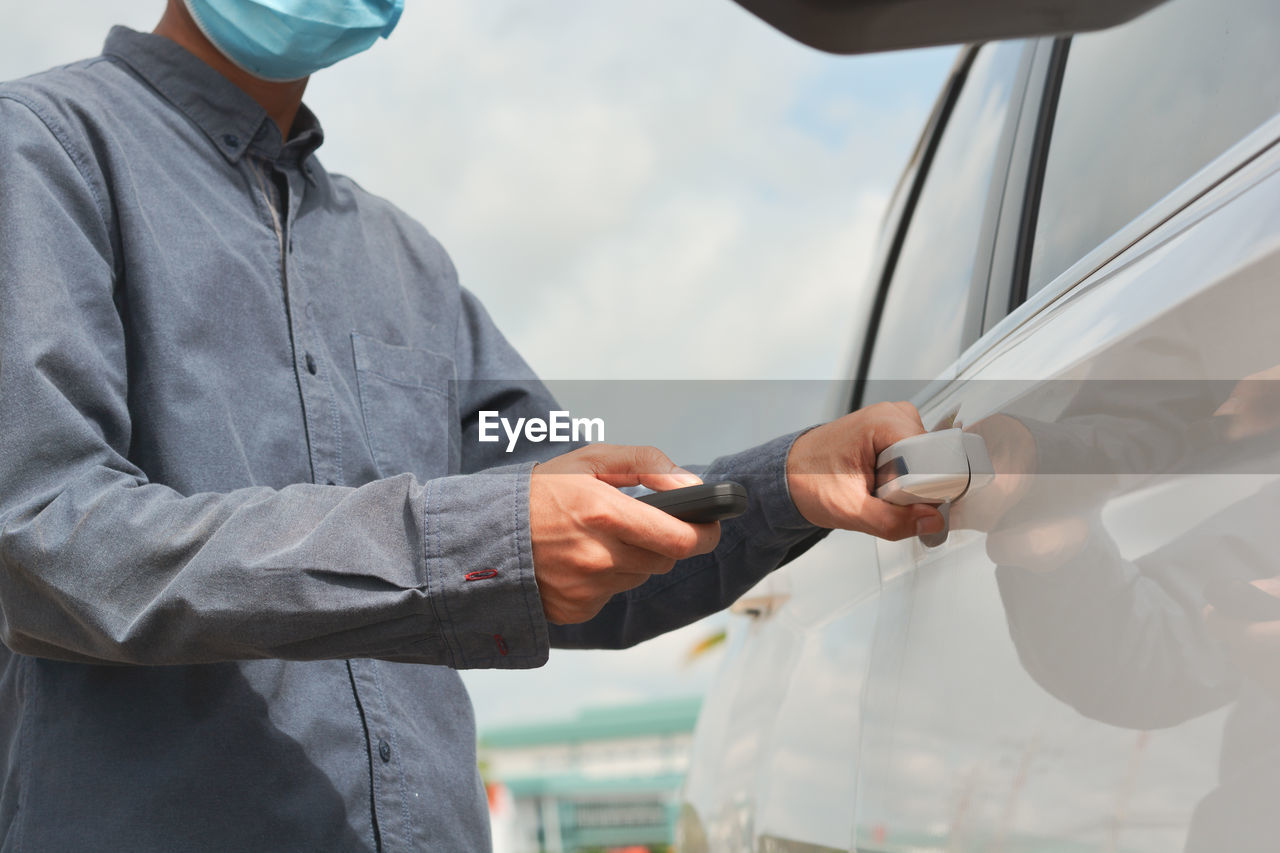 REAR VIEW OF MAN HOLDING CAMERA WHILE STANDING BY CAR ON MIRROR