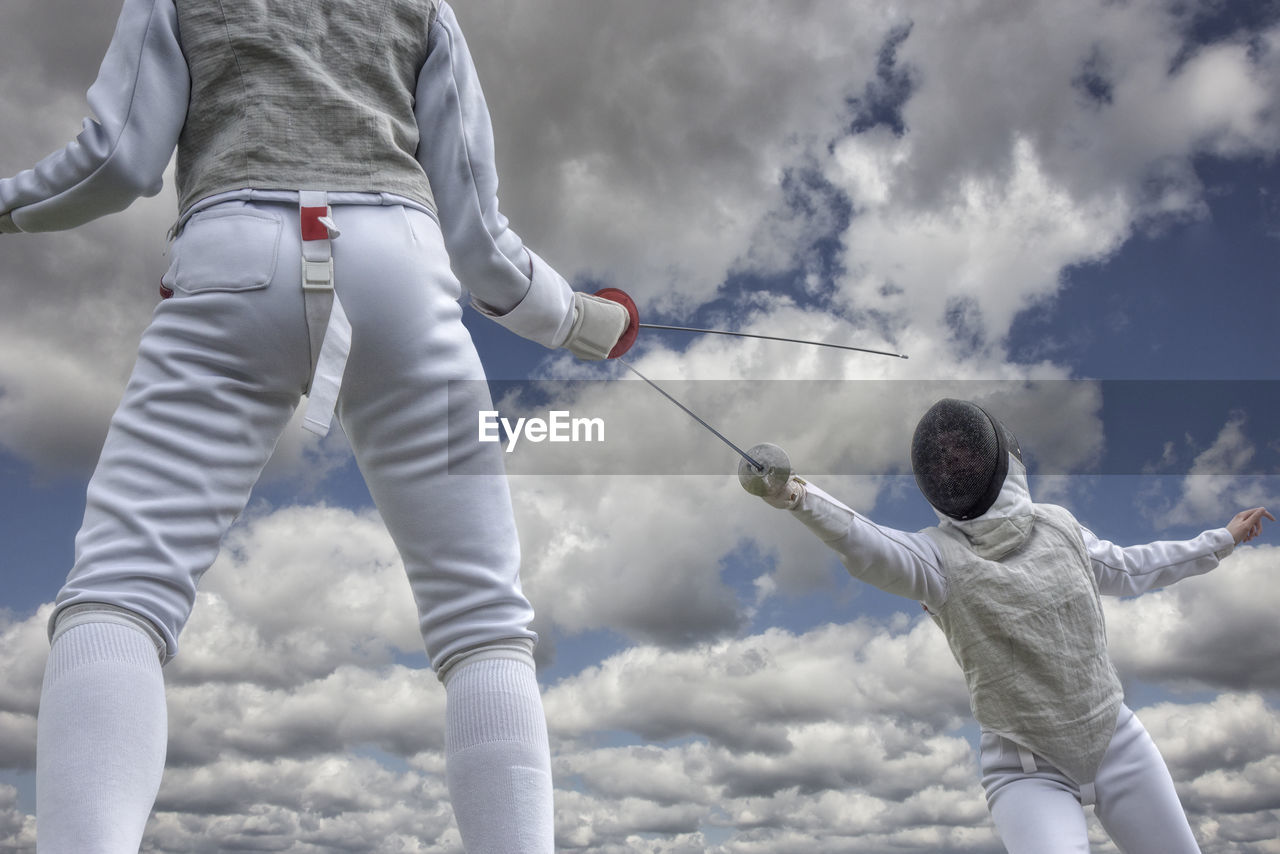 Low angle view of people fencing against sky