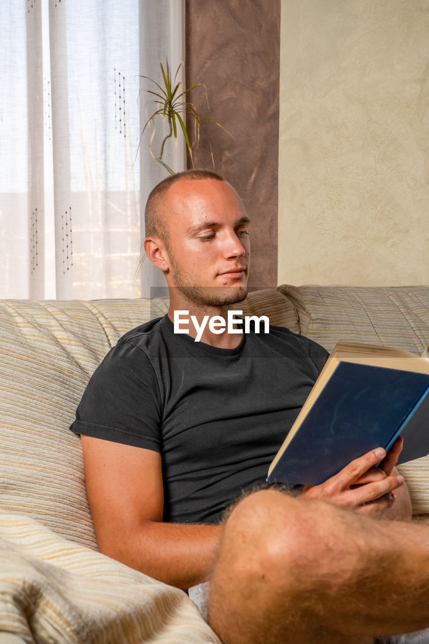 MAN LOOKING AT CAMERA WHILE SITTING ON TABLE AT HOME