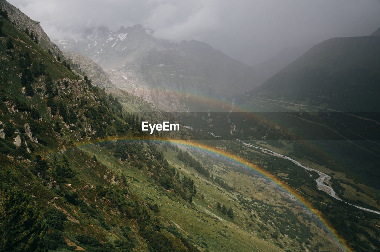 Scenic view of mountains with rainbow against sky