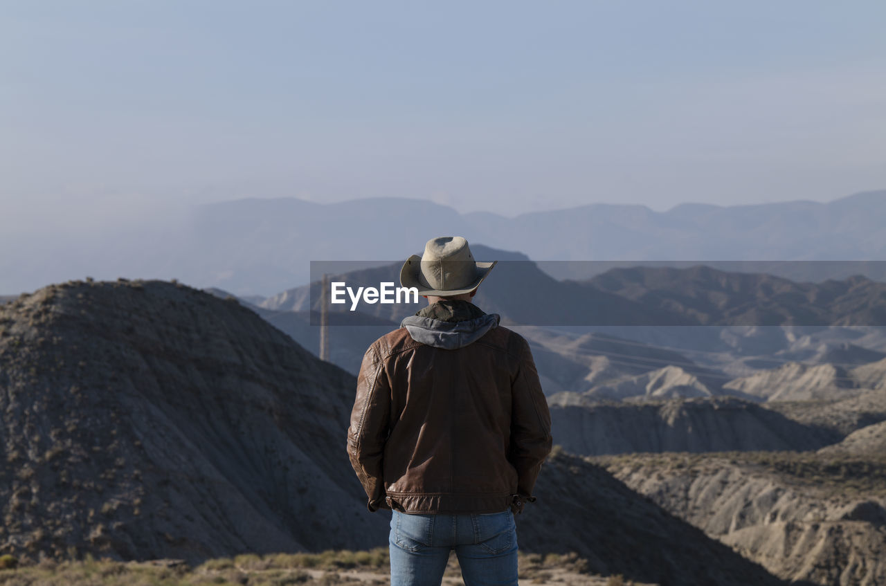 Rear view of adult man in cowboy hat looking at view of tabernas desert, almeria, spain