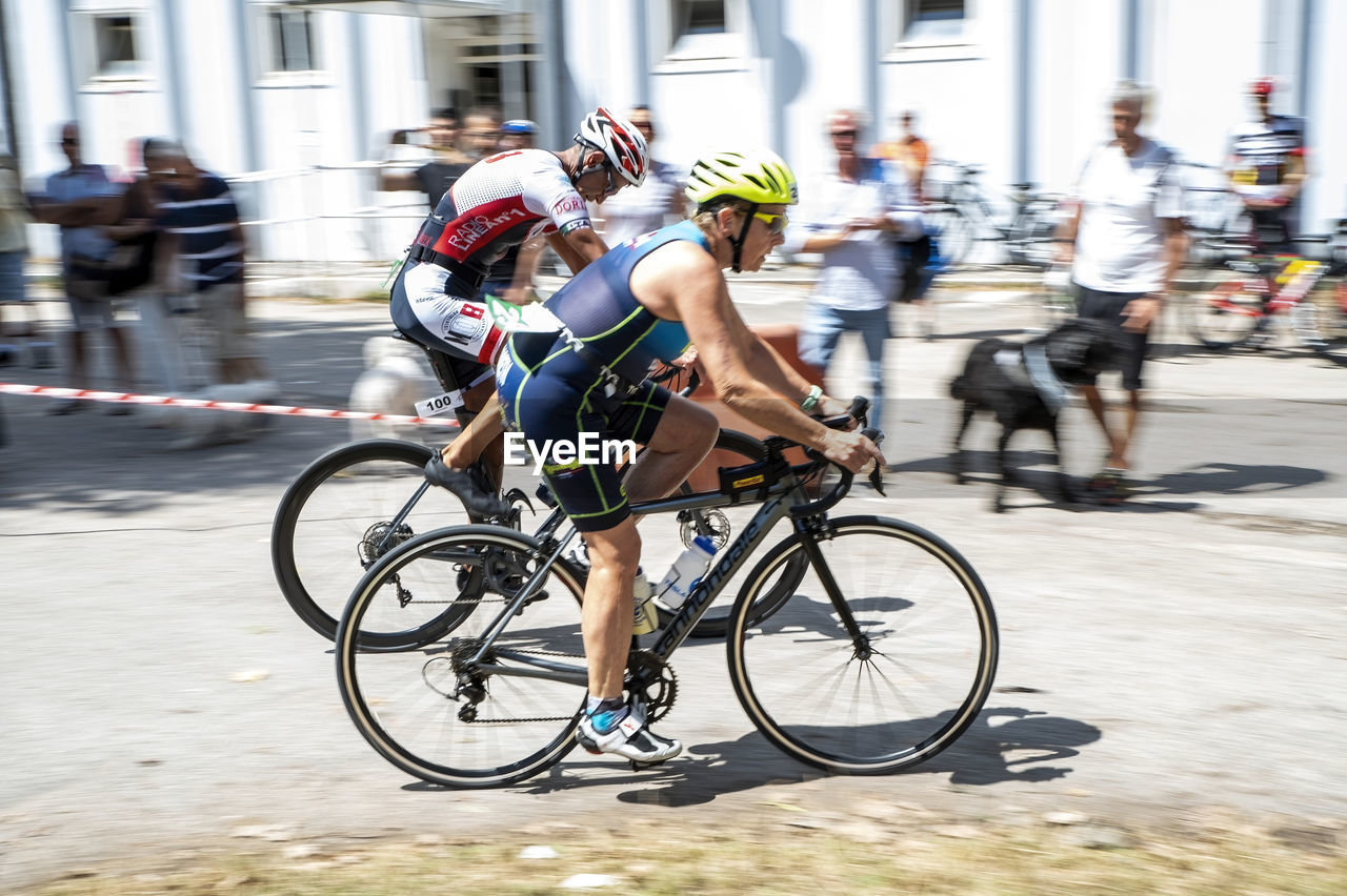 bicycle, transportation, sports, activity, cycling, road bicycle, road cycling, road bicycle racing, motion, racing bicycle, group of people, city, endurance sports, architecture, adult, bicycle racing, street, vehicle, men, race, sports equipment, lifestyles, mode of transportation, city life, blurred motion, city street, competition, recreation, road, cycle sport, riding, speed, crowd, footwear, person, large group of people, women, sports race, clothing, headwear, helmet, bicycle helmet, full length, wheel, exercising, on the move, building exterior, bicycle wheel, outdoors, athlete