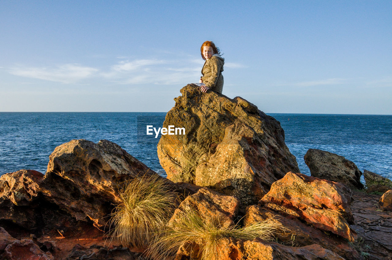 Girl sitting on rock by sea against sky