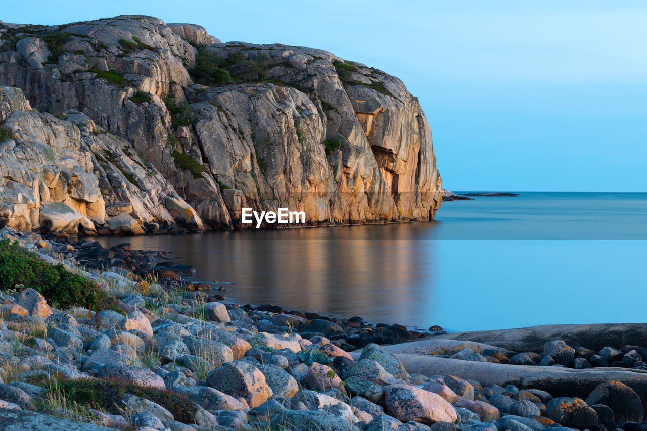 Scenic view of rocks by sea against sky