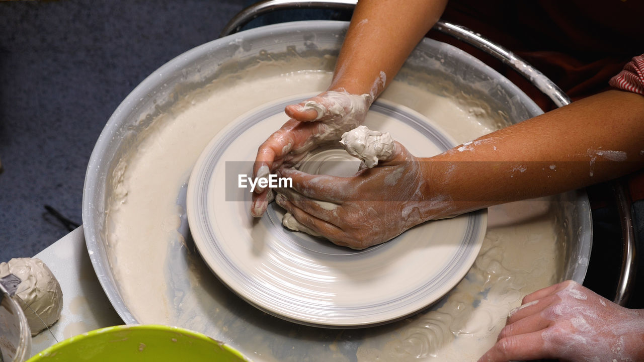 A woman working at a potter's wheel in the workshop. close-up of potter's hands stained with clay
