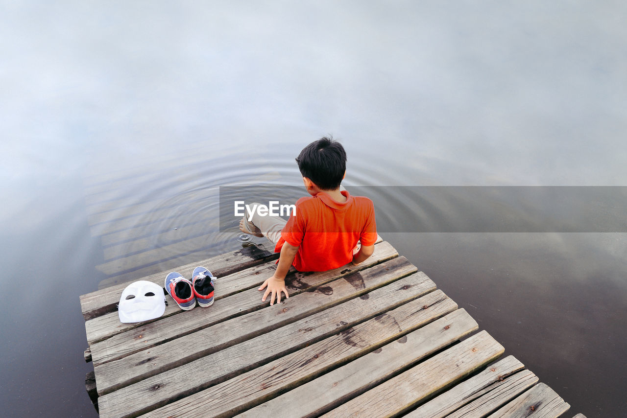 Rear view of boy sitting by lake on jetty