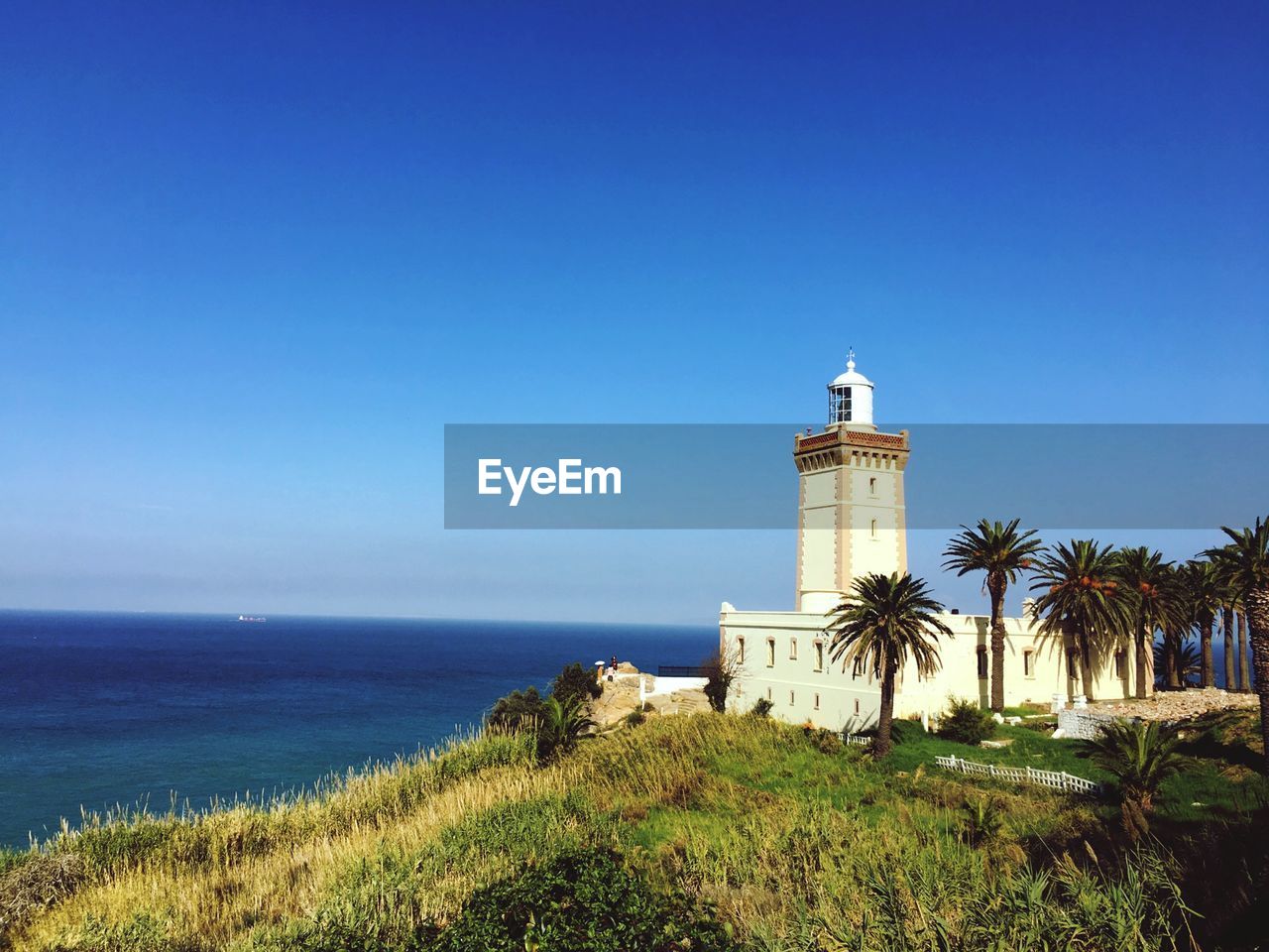 Lighthouse by sea against clear sky