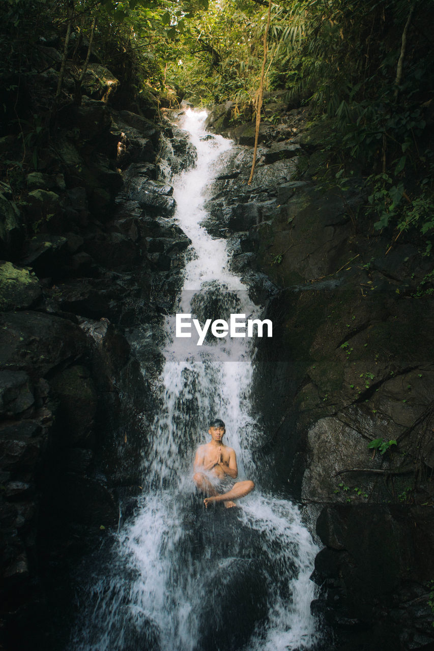 Man sitting on rock amidst waterfall