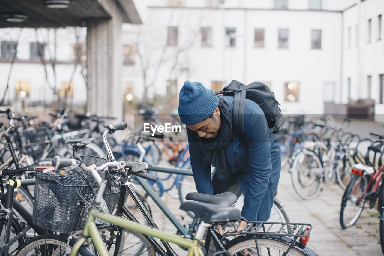 Young male university student unlocking bicycle in campus