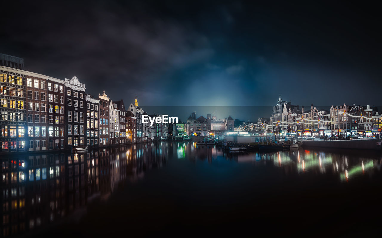 Illuminated buildings by river against sky in city at night