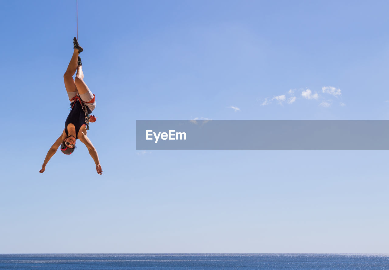 Woman hanging over sea against sky