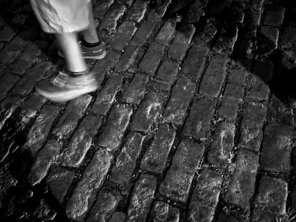 Low section view of man standing on brick pavement at night
