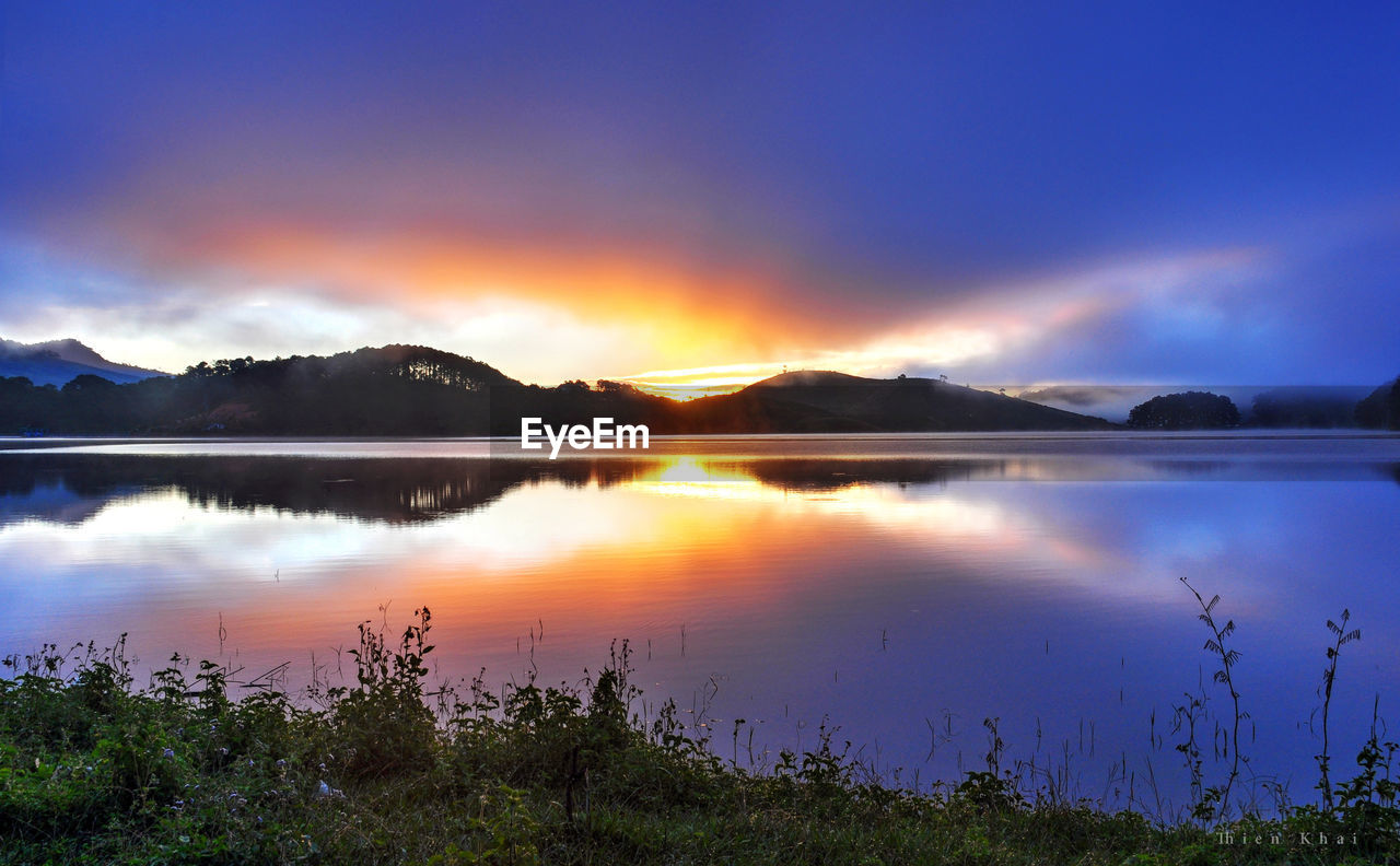 SCENIC VIEW OF LAKE BY SILHOUETTE MOUNTAINS AGAINST SKY AT SUNSET