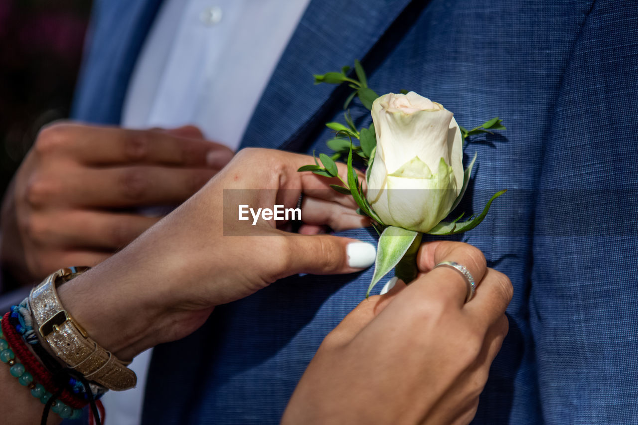 Close-up of hands attaching rose on blazer