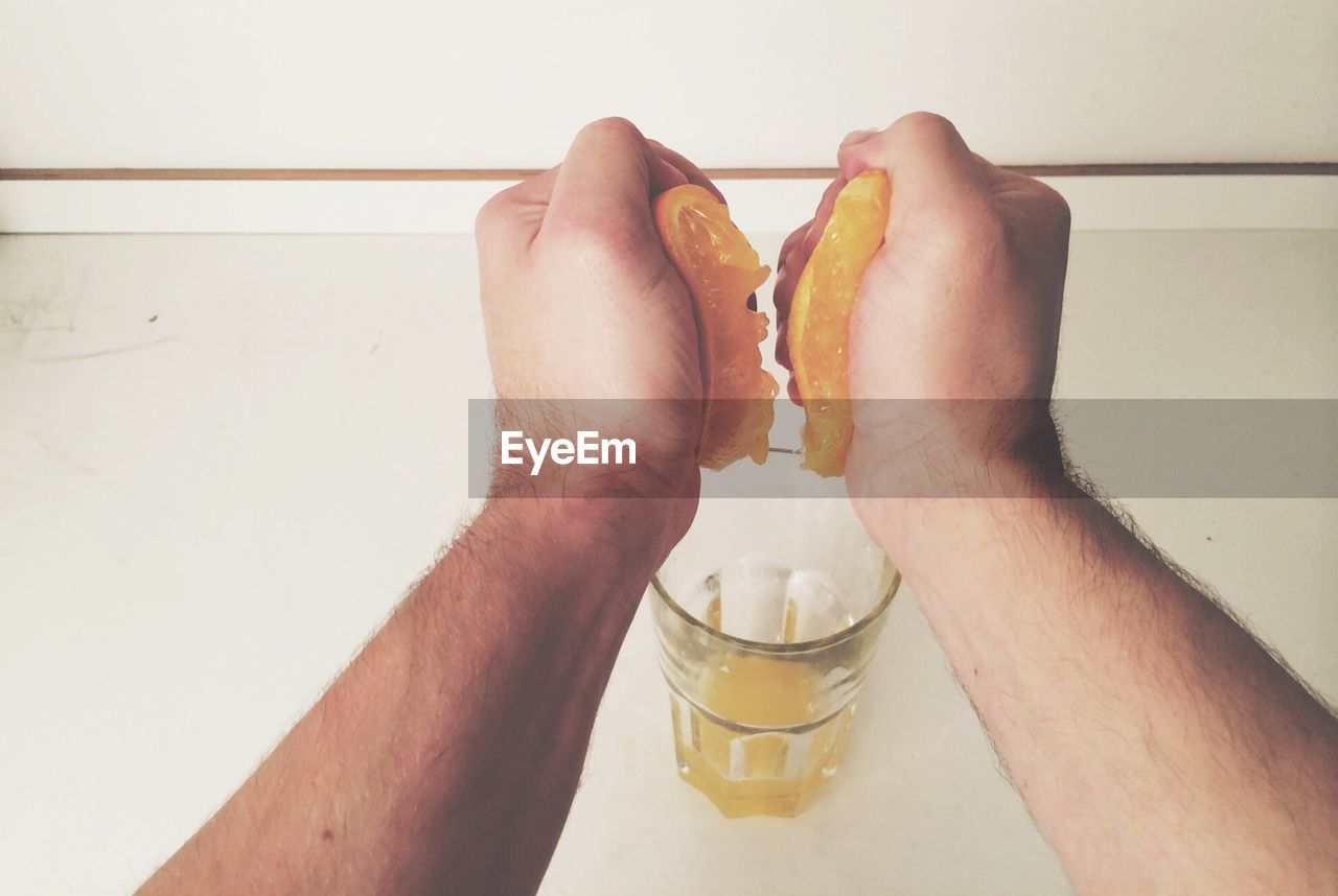 Cropped image of person squeezing orange juice in drinking glass