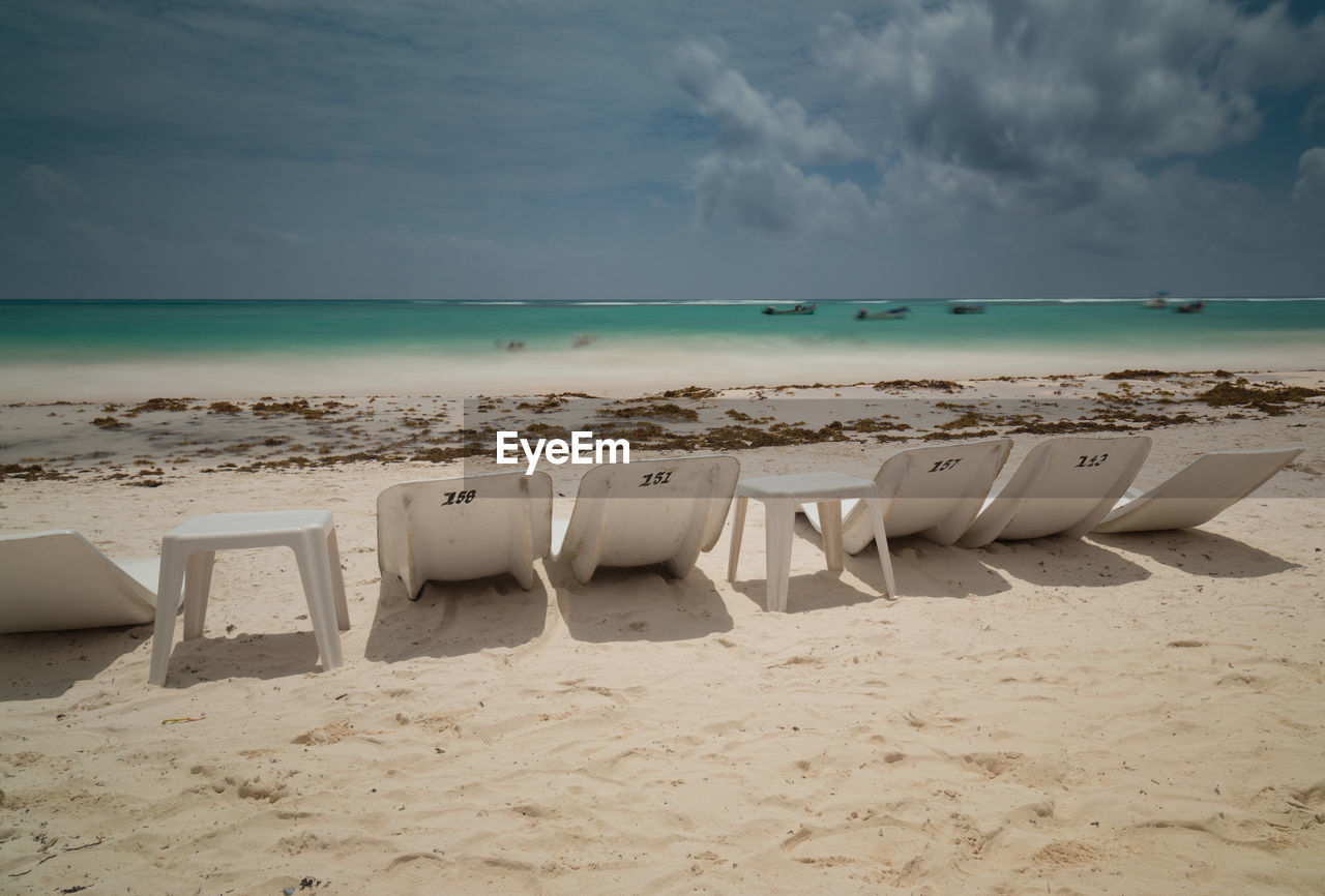 LOUNGE CHAIRS ON BEACH AGAINST SKY