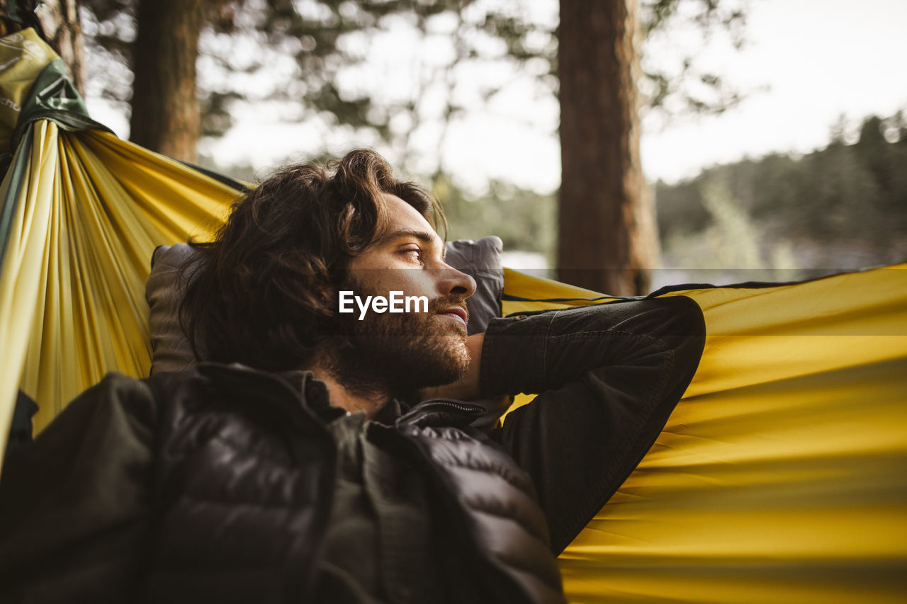 Contemplating man looking away while lying over hammock in forest