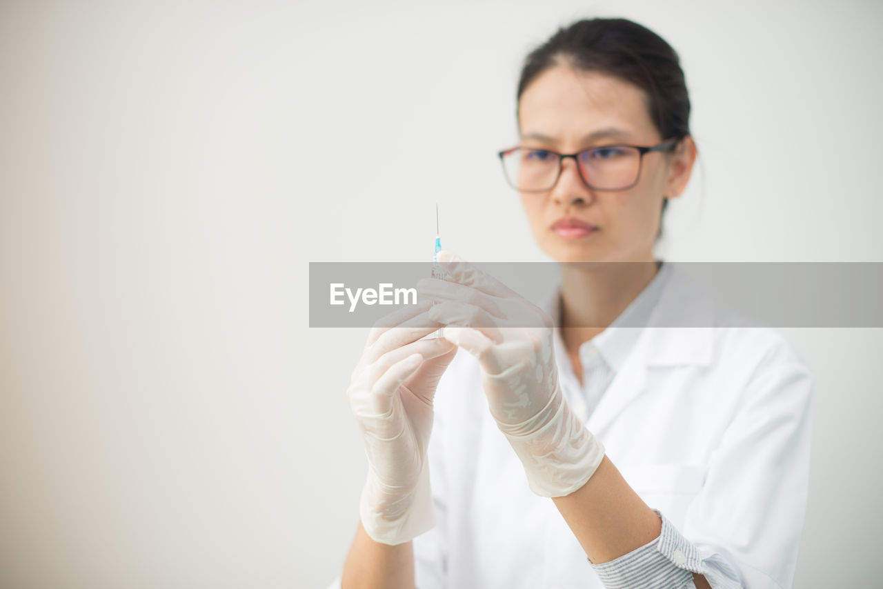 Close-up of doctor holding syringe against gray background