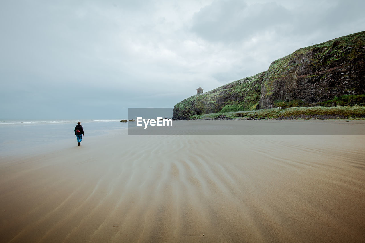 Rear view of woman walking at beach against sky