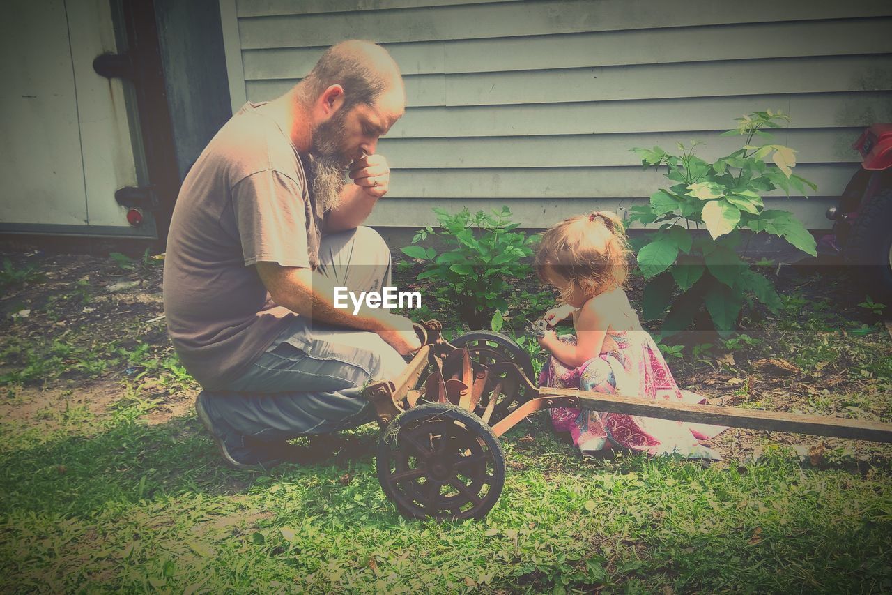 Father and daughter crouching on field at backyard