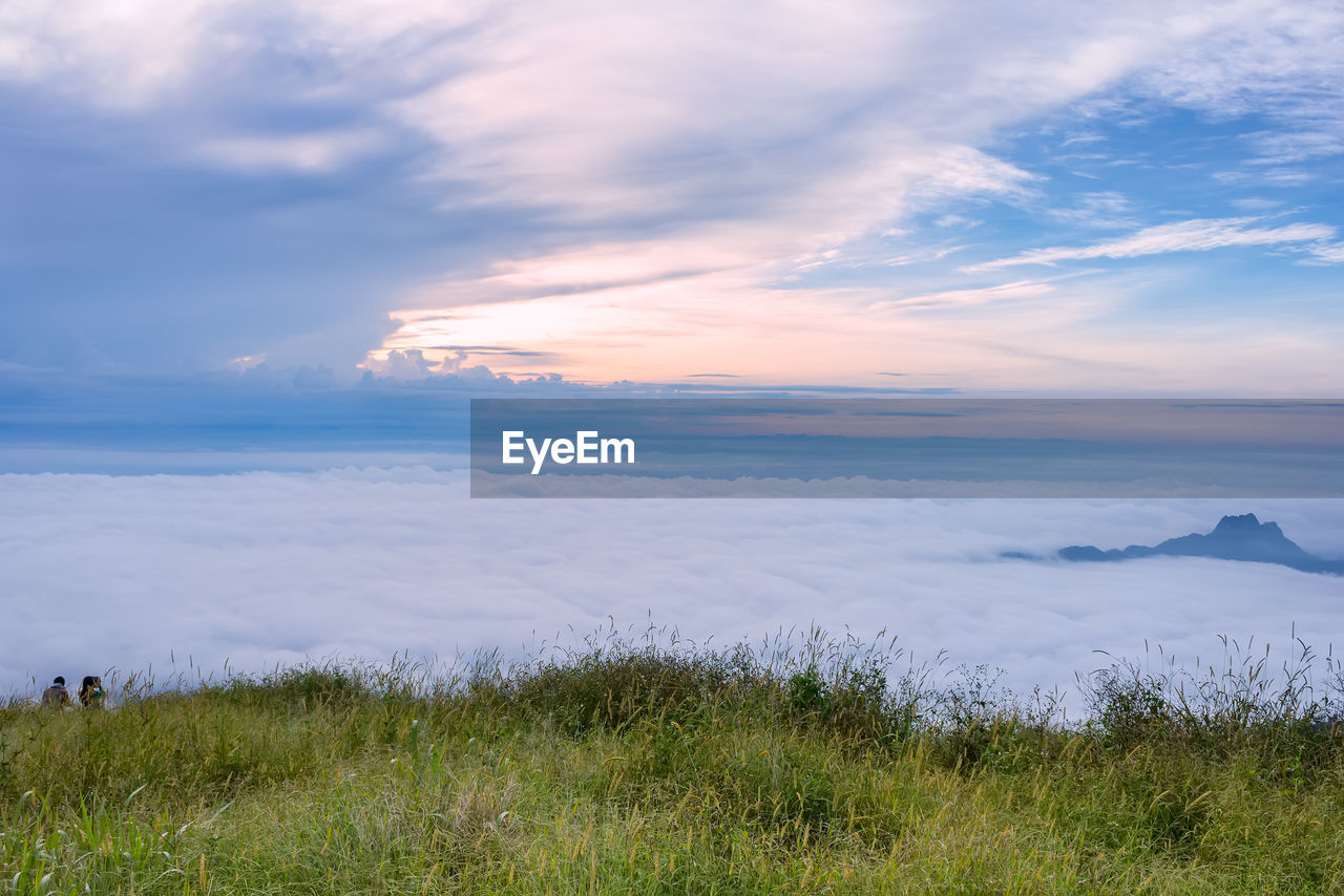 Friends standing on grassy field against cloudy sky during sunset