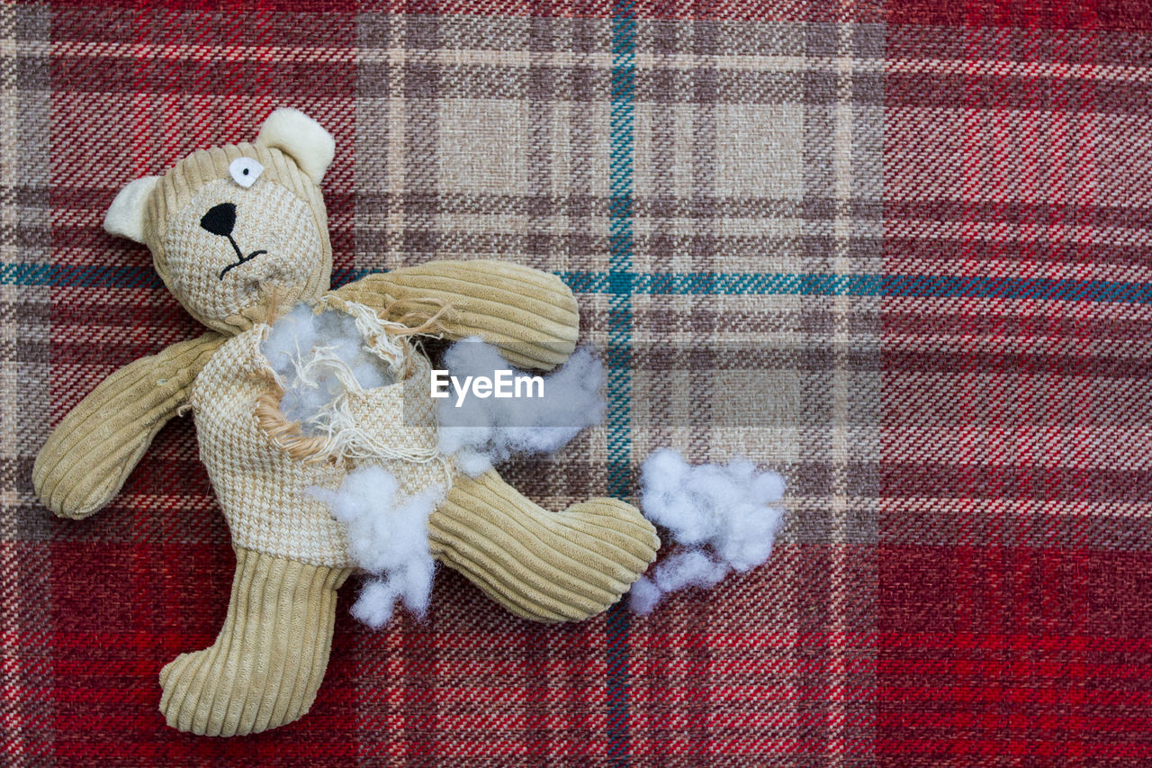 A sad and abandoned teddy bear with stuffing and filling falling from a ripped and torn hole 