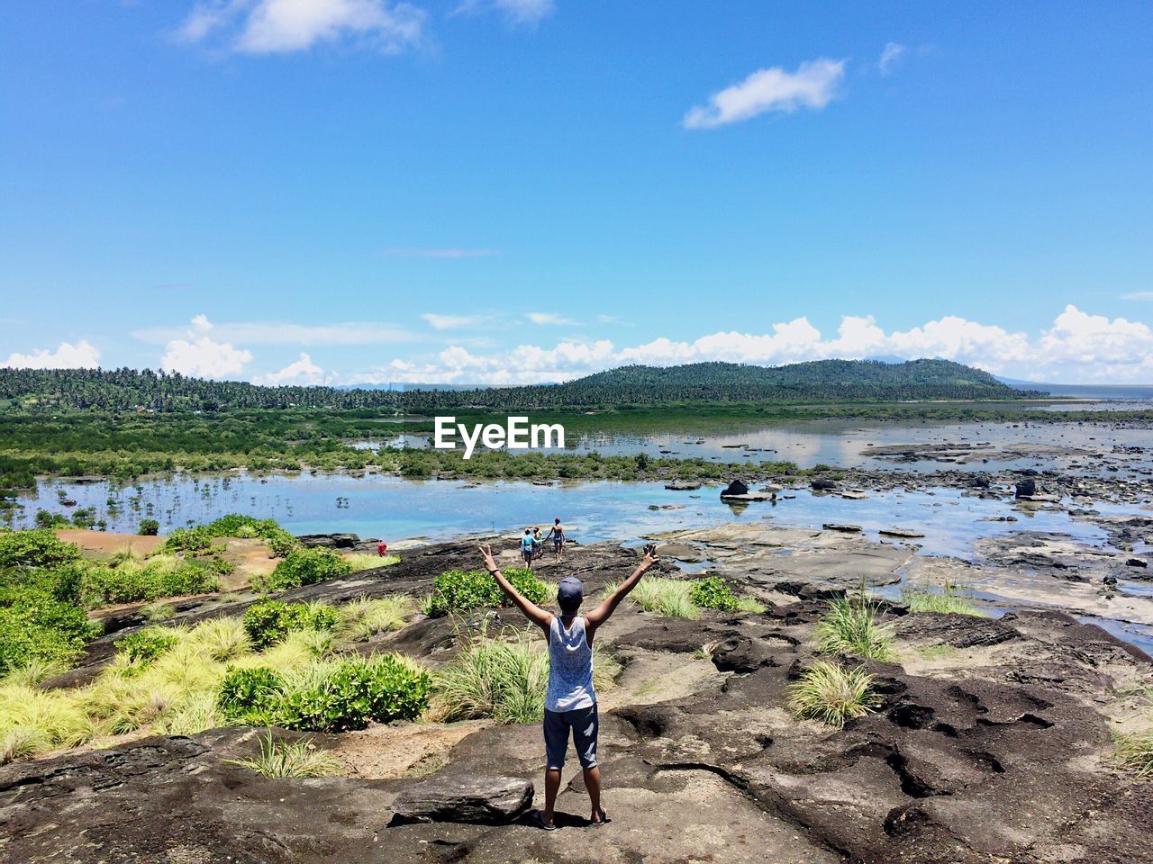 Rear view of man with arms raised standing by lake