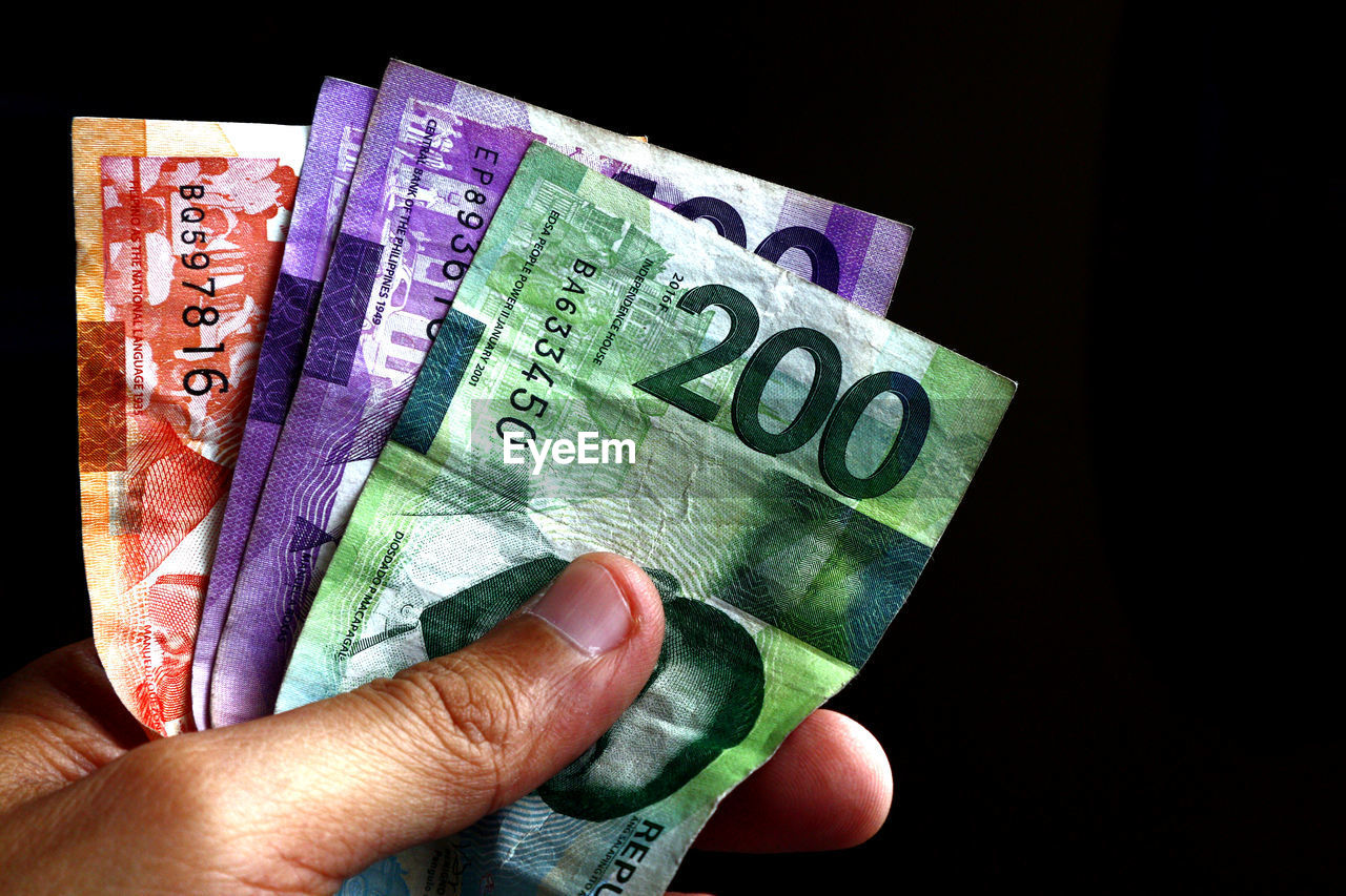 Close-up of hand holding paper currency against black background