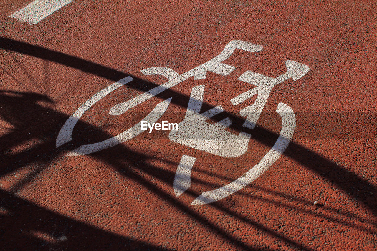 Signage on the cycle path, ocher-colored road surface, shadow of a bicycle.