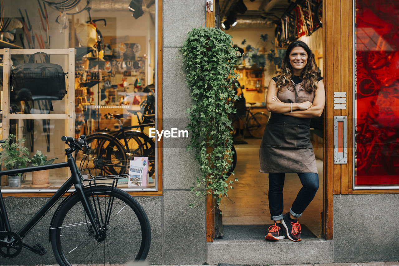Portrait of female expertise with arms crossed standing on doorway of bicycle shop