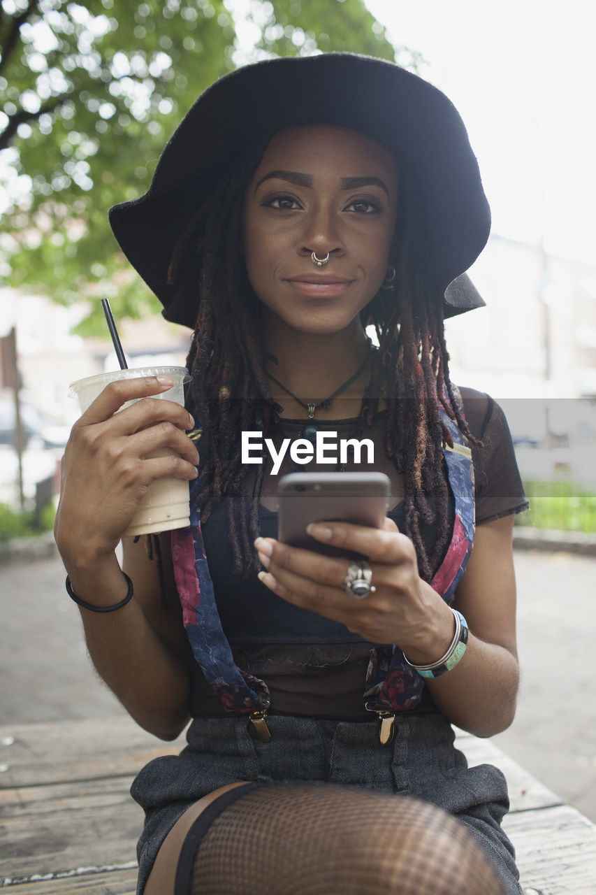 A young woman on her cell phone whilst holding an iced coffee.