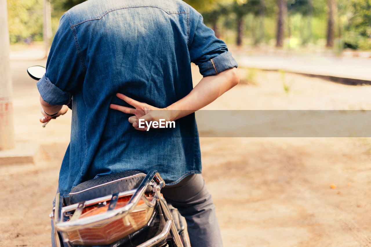 Midsection of man gesturing peace sign while riding motorcycle