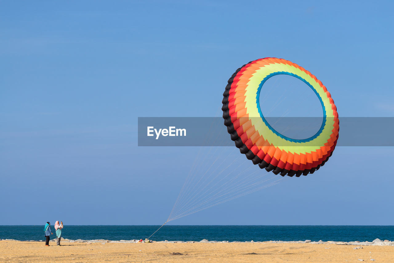Low angle view of large colorful kite flying over beach against clear blue sky