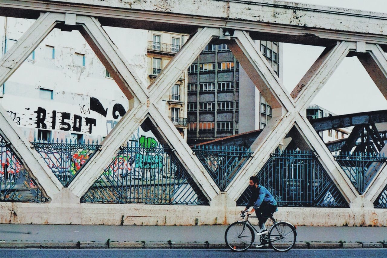 MAN RIDING BICYCLE ON BRIDGE