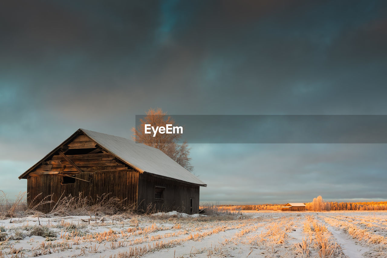 Barn on landscape against cloudy sky during winter